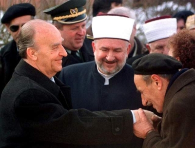  Drugi dan Ramazanskog bajrama &bdquo;Dan &scaron;ehida&ldquo;, 30. januar, 1998. godine: Jedan obični džematlija ljubi ruku rahmetli predsjedniku Aliji Izetbegoviću. Na fotografiji su i: reisul-ulema Mustafa Cerić, rahmetli general Rasim Delić, rahmetli hafiz Ismet Spahić, zamjenik reisul-uleme rahmetli Muharem Hasanbegović, &scaron;ef Kabineta reisululeme i predsjednik Udruženja ilmijje, na &scaron;ehidskom mezarju Kovači.